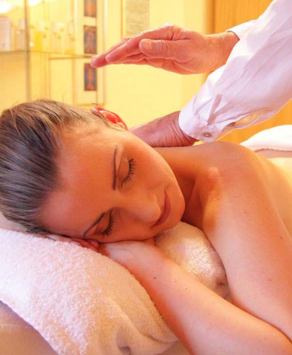 Entspannende Nackenmassage Eine Frau liegt entspannt auf einer Massageliege, die Augen geschlossen, während eine Person ihre Nacken- und Schulterpartie sanft massiert. Der Raum ist in warmes Licht getaucht.